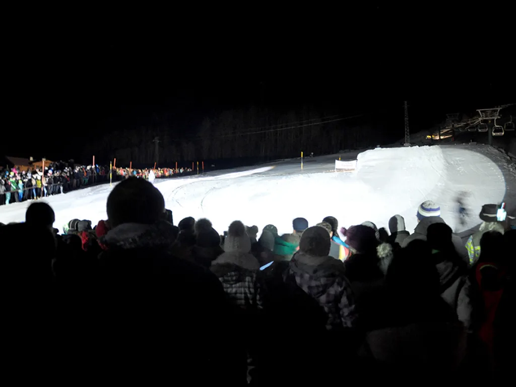 Zuschauer stehen abends vor der beleuchteten Piste.